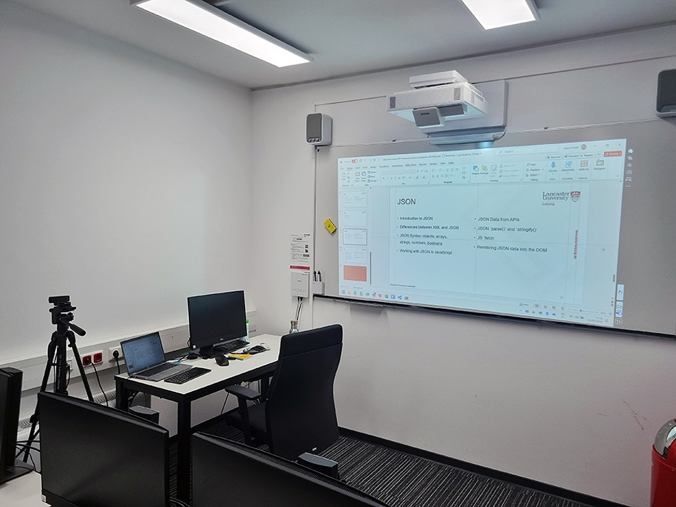 Classroom in Leipzig with a projected Computer Ecosystems lecture slide on JSON: syntax, fetch, and rendering data into the DOM